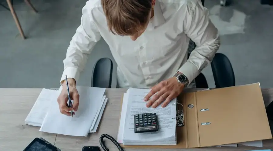 Man in an office reviewing financial papers with a calculator on a desk.