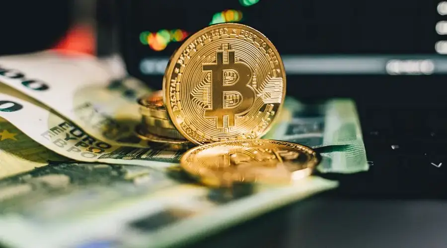 Close-up of Bitcoin and Euro notes on laptop keyboard with market chart in background.