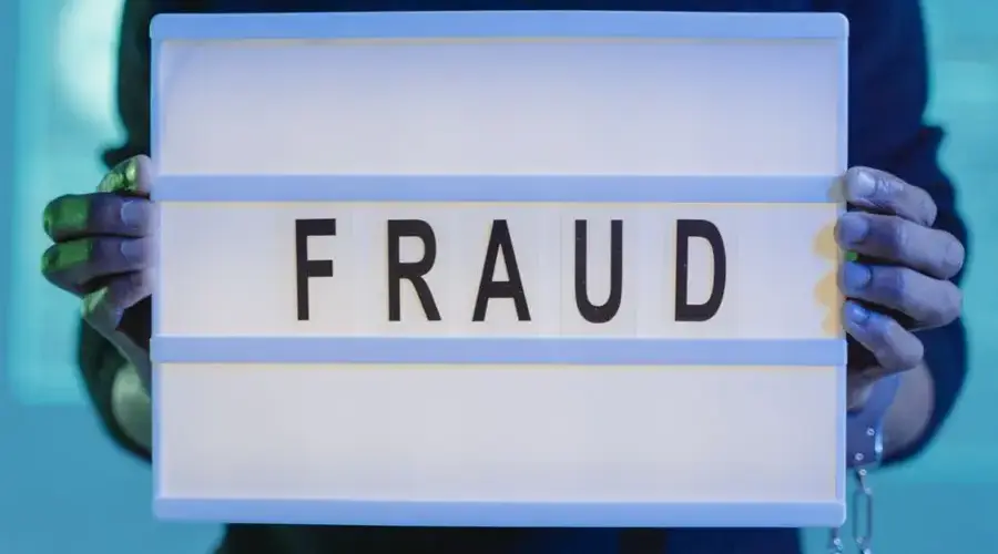 Close-up of hands holding a sign with 'fraud', illuminated in blue light.