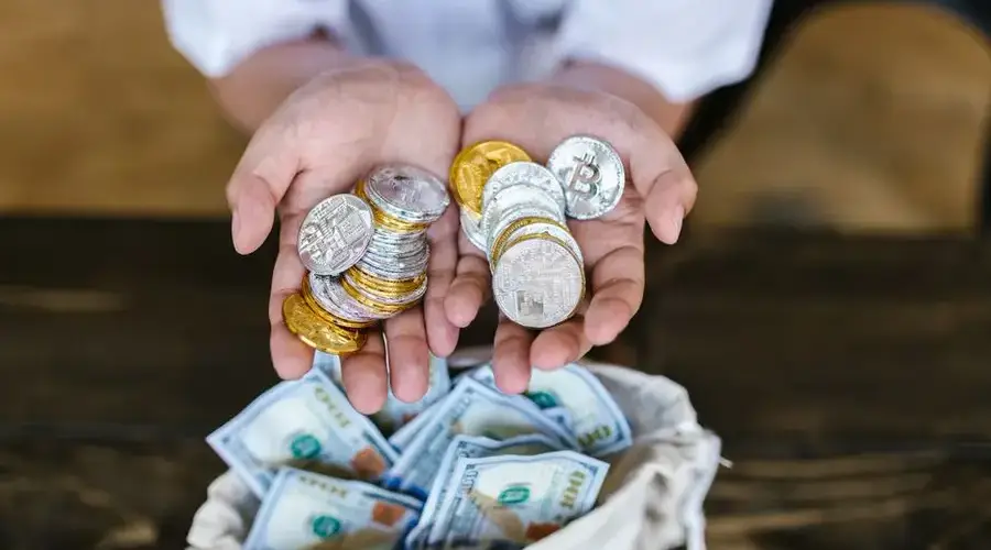 Person holding cryptocurrency coins above a bag of cash, symbolizing digital and traditional finance intersections.