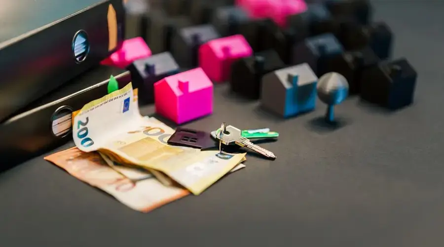 Miniature houses, euro bills, and a house key symbolize real estate investment and property transactions.