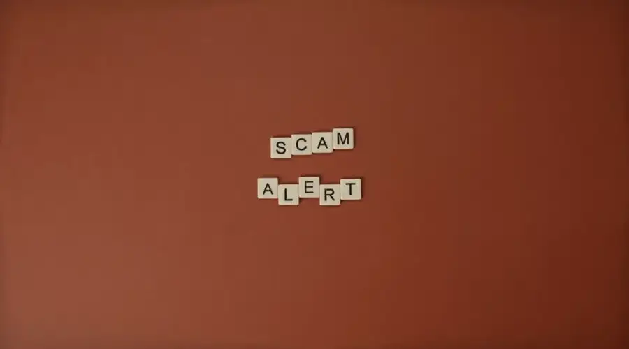 Scrabble tiles spelling Scam Alert on a brown surface indicating caution.