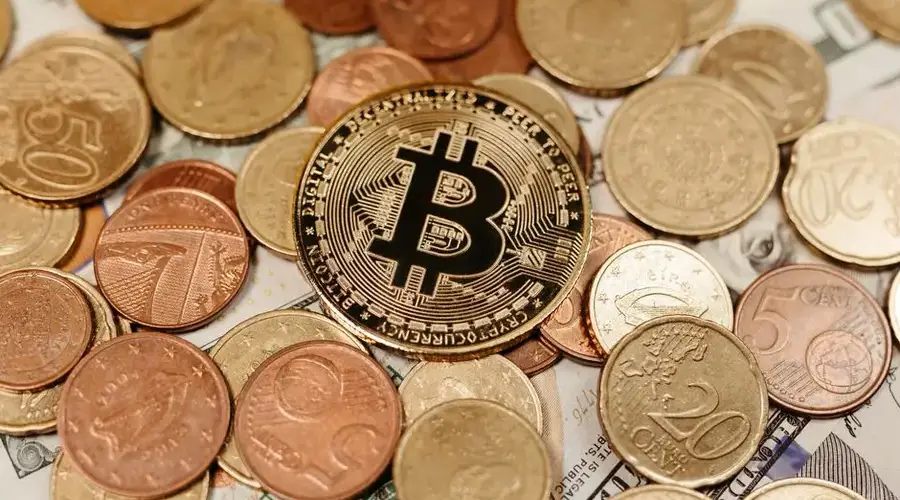 A Bitcoin coin lies on top of various euro and dollar coins, symbolizing digital currency and financial diversity.