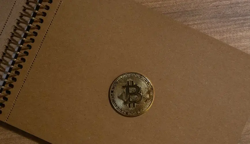 Close-up of a Bitcoin gold coin on a brown notebook, representing finance and cryptocurrency concepts.