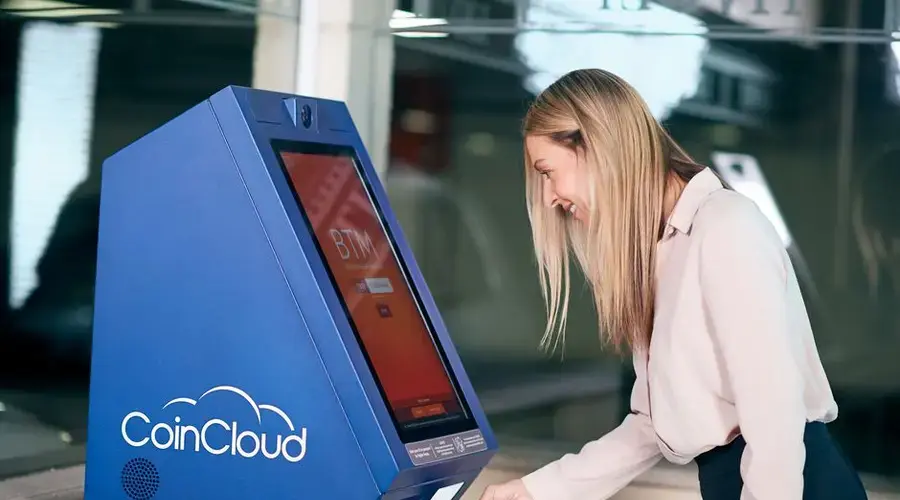 Woman smiling while using a CoinCloud cryptocurrency ATM indoors.