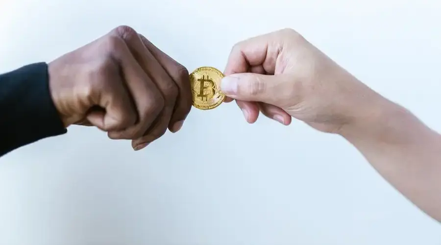 Two hands exchanging a Bitcoin coin, symbolizing cryptocurrency transactions.