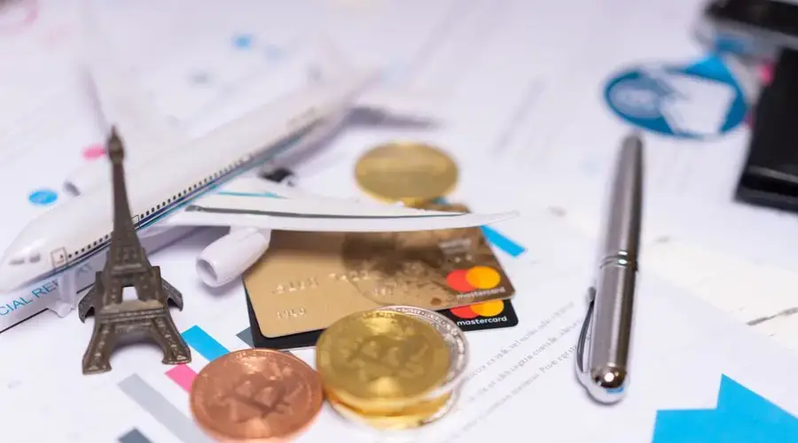 A travel finance concept featuring cryptocurrency, credit card, airplane model, and Eiffel Tower on financial documents.