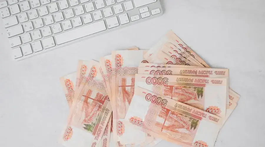 Pile of 5000 ruble banknotes next to a keyboard on a white surface, viewed from above.
