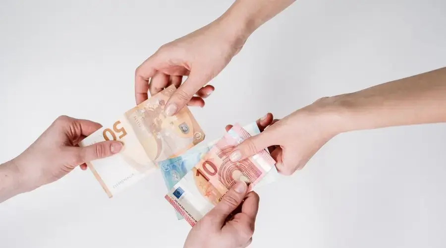 Two pairs of hands exchanging Euro banknotes, symbolizing finance and transaction.
