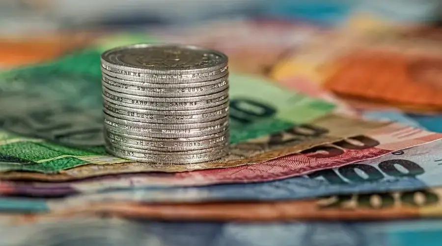 A stack of coins on top of various colored banknotes, symbolizing finance and currency.