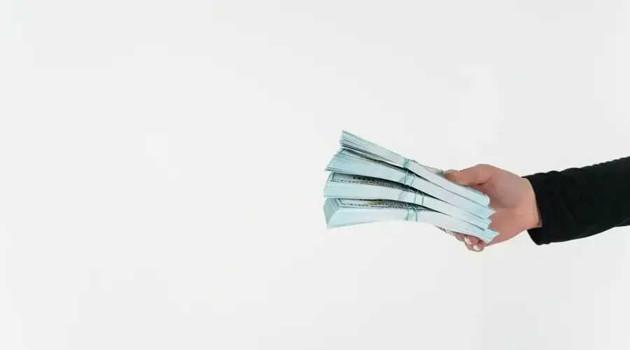 Close-up of a hand holding bundles of American dollar bills against a white background.