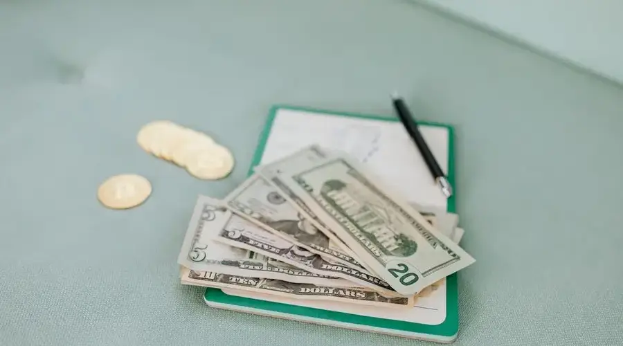 Close-up of American dollar bills and coins on a journal with a pen, representing budget planning.
