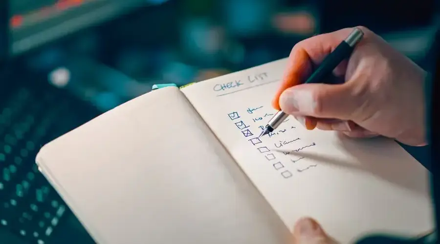Close-up of a hand writing in a notebook with a checklist for effective task management.