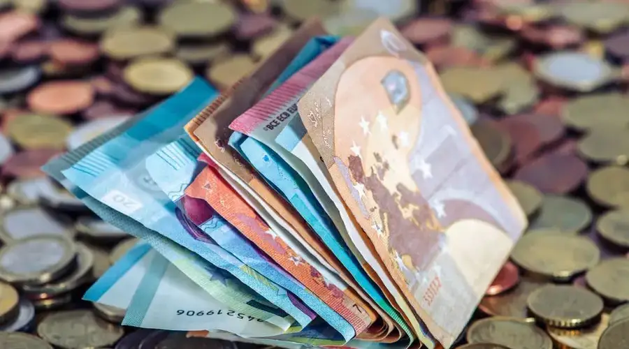A stack of euro banknotes and scattered coins symbolize wealth and finance.