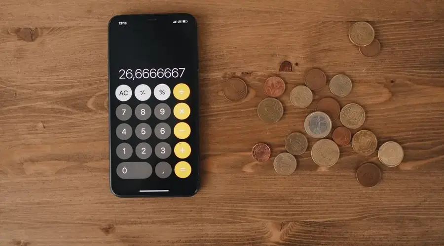 Overhead view of a smartphone calculator with European coins on a wooden surface, symbolizing modern finance.