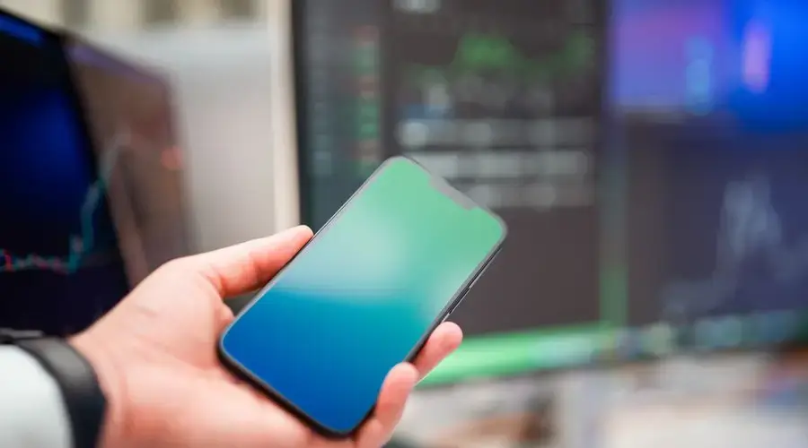 A person holding a smartphone with forex charts displayed, implying modern finance and technology.