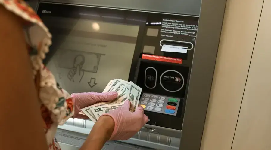 A person wearing gloves withdraws cash from an ATM, ensuring hygiene.
