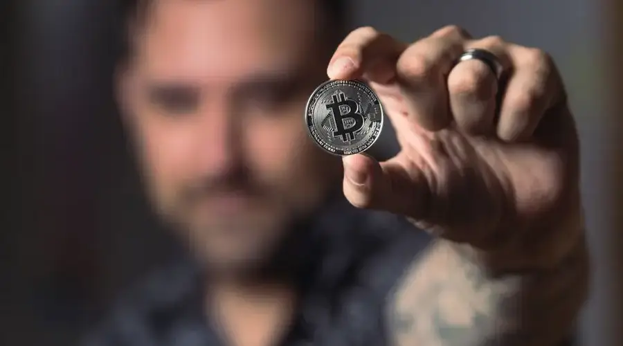 Adult male hand holding a Bitcoin, showcasing cryptocurrency focus indoors.