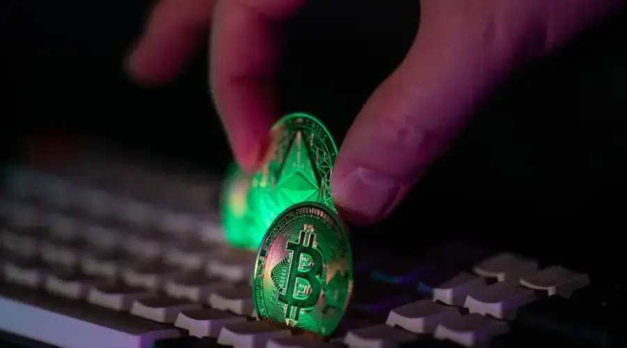 Close-up of a hand placing bitcoin and ethereum coins onto a computer keyboard, symbolizing cryptocurrency and digital finance.