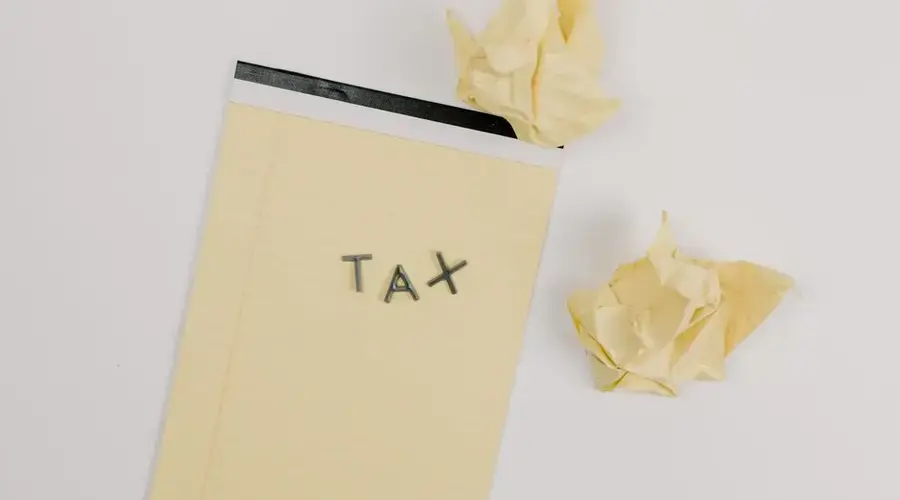 Flat lay of a notepad labeled 'tax' with crumpled paper on a white background, symbolizing financial stress.