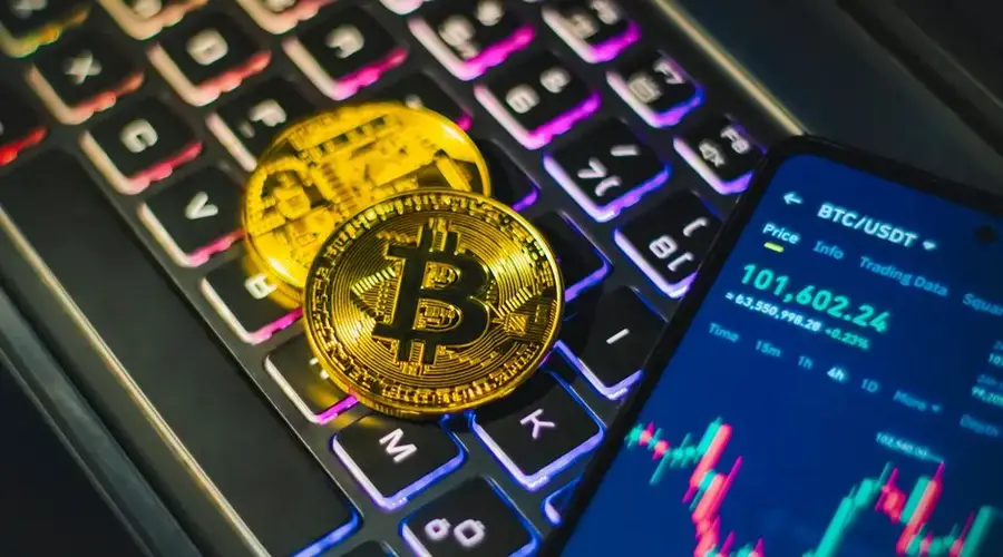 Close-up of gold Bitcoin coins on a backlit keyboard with trading app on smartphone.