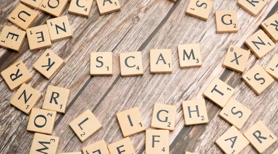 Scrabble tiles on a wooden background spell out the word 'scam', concept for deception and trickery.