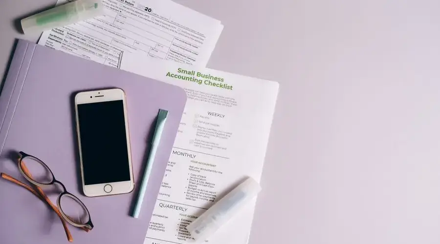 Flat lay of accounting documents, smartphone, and glasses on a desk.