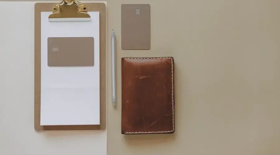 Flat lay of a minimalist office desk with clipboard, credit cards, pen, and leather wallet.
