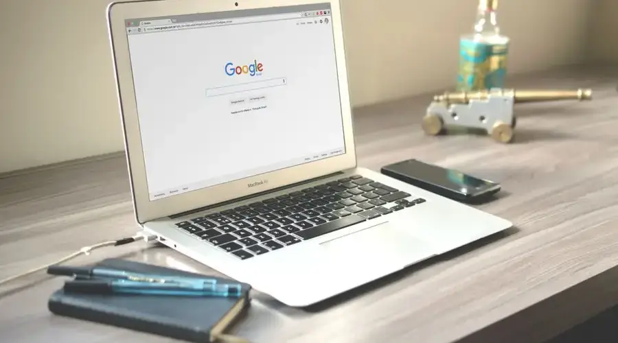 A neat workspace featuring a laptop displaying Google search, a smartphone, and a notebook on a wooden desk.