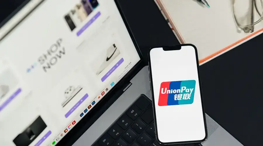 UnionPay logo displayed on a smartphone next to a laptop with an online shopping page open.