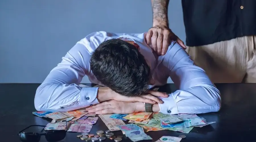 Depressed man surrounded by Argentine pesos represents financial stress and burnout.