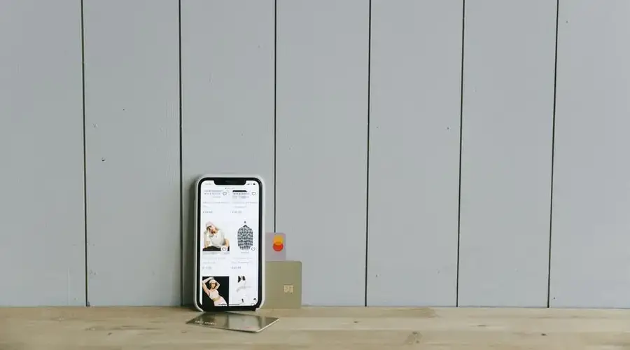 A smartphone displaying an ecommerce site with a credit card, set on a wooden surface, depicting online shopping.