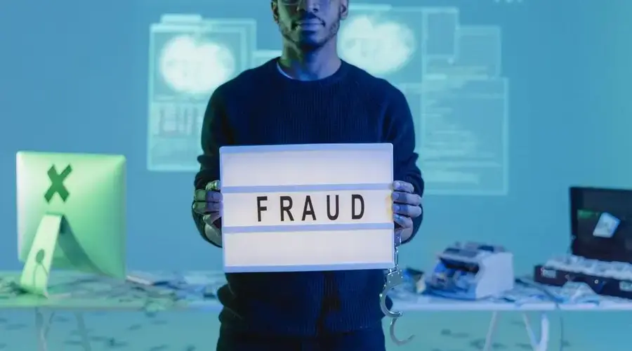 Man holding a 'FRAUD' sign in a tech setting, symbolizing cybersecurity threats.