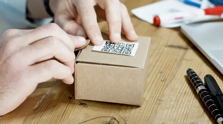 Close-up of hands packing a box with a QR code, symbolizing online business services.