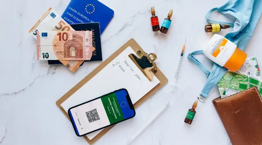 Flat lay of travel essentials including vaccination passport, euros, and medical supplies.