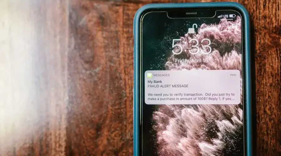 Close-up of a smartphone displaying a fraud alert notification on a wooden surface.