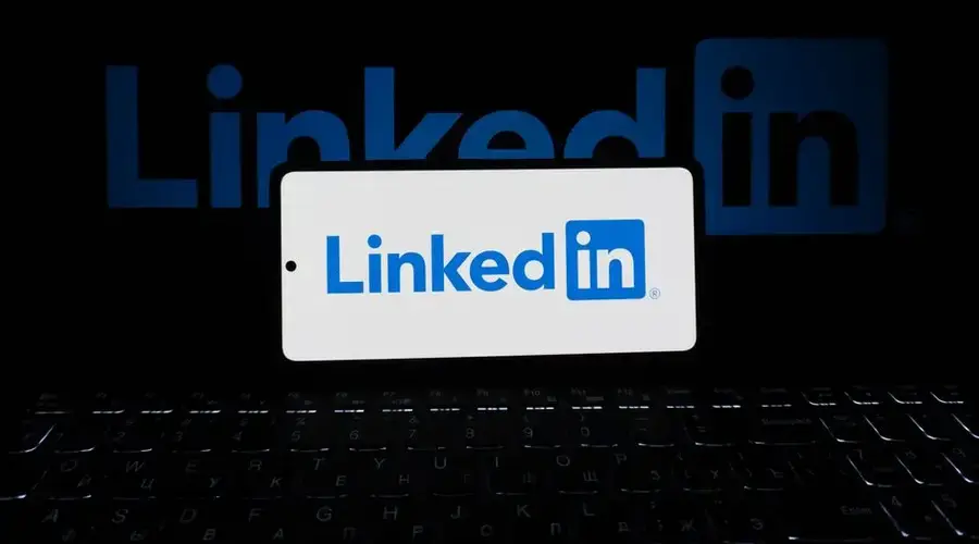 Smartphone showing LinkedIn logo with keyboard and large background logo, business theme.