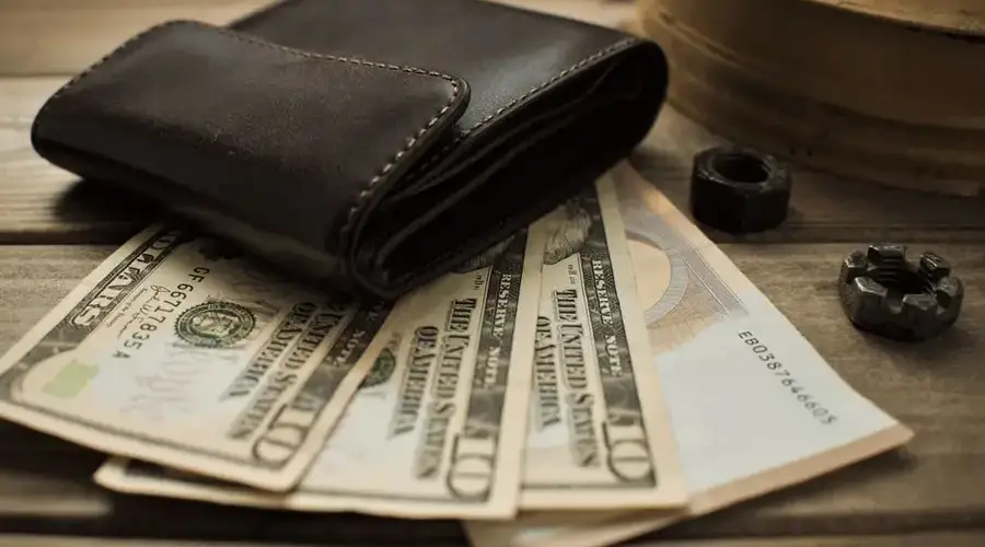 Close-up view of a leather wallet with US dollar bills on a wooden table.