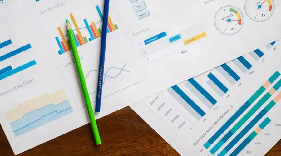 Flat lay of various business charts and colored pencils on wooden table, highlighting financial analysis.