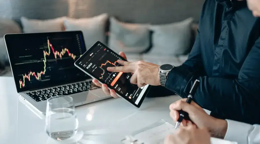 Professionals analyzing financial data on a tablet and laptop in an office setting.