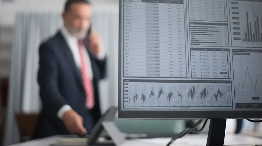Professional analyzing financial and stock market data on a computer screen in an office setting.