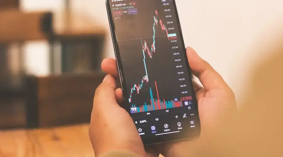 Person holding smartphone with stock market graph, portraying financial trends.