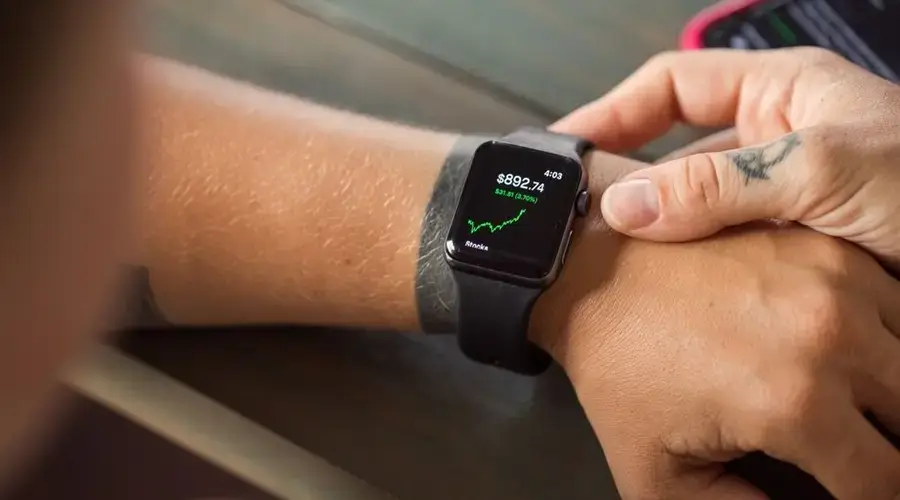 Close-up of a smartwatch showing stock market data, with hands wearing it.