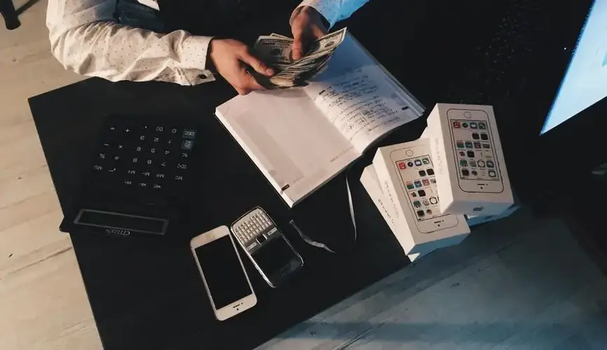 Businessman organizing finances with tech devices and cash on desk.