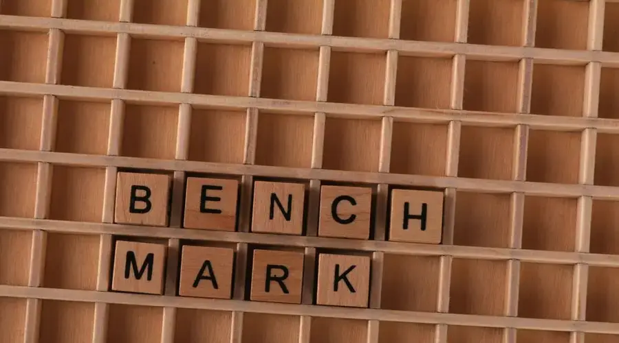 Wooden letter tiles spelling 'BENCHMARK' placed on a grid-like wooden background.