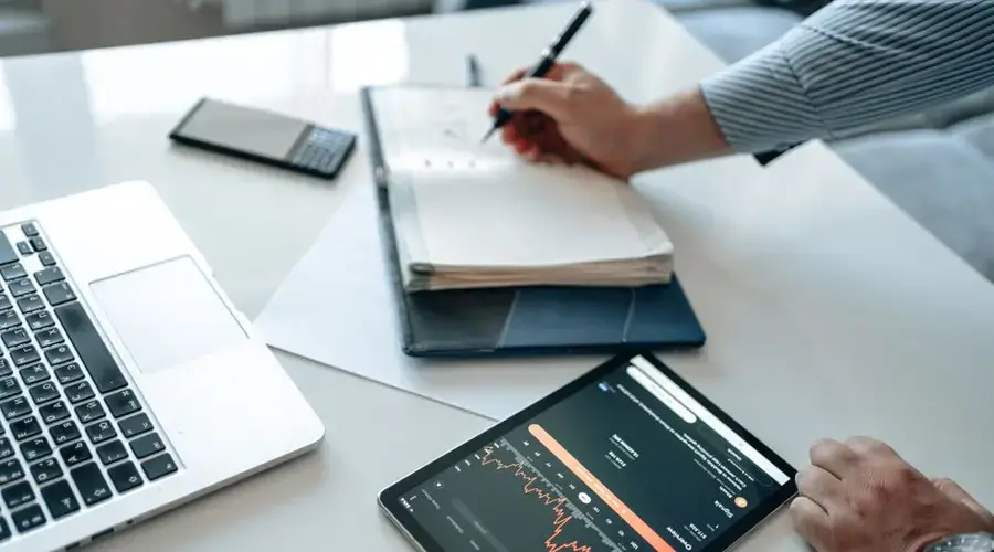 Close-up of a business professional analyzing data trends using a tablet and laptop.