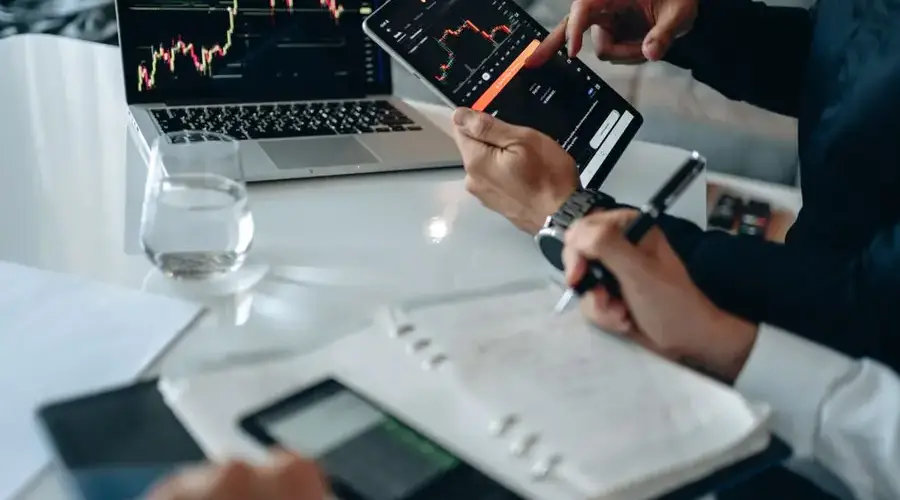 Business professionals reviewing financial charts on digital devices in a modern office setting.