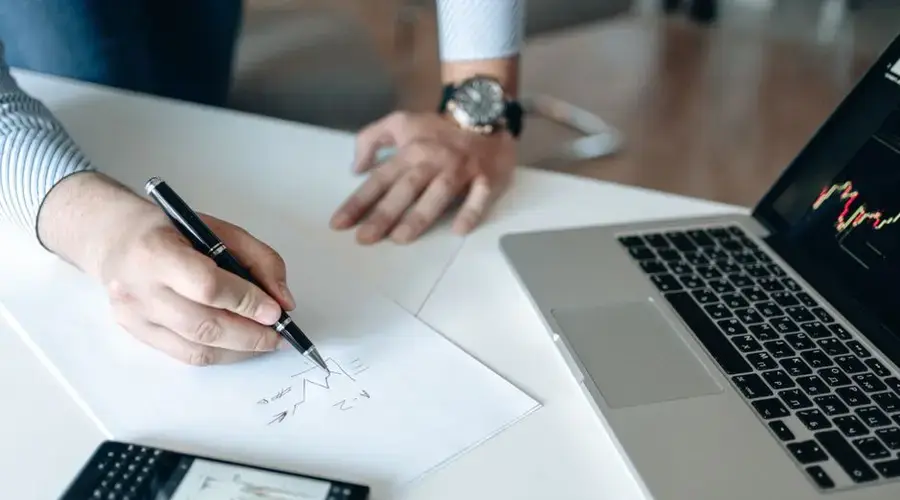 A professional analyzing financial graphs on paper and a laptop, showcasing business strategy.