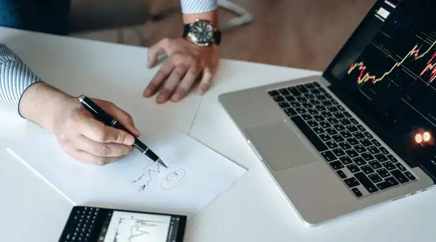 Professional workspace with financial analysis on laptop, smartphone, and paper.