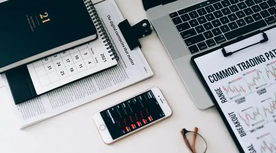 Home office desk featuring trading charts, smartphone, and laptop for financial analysis.